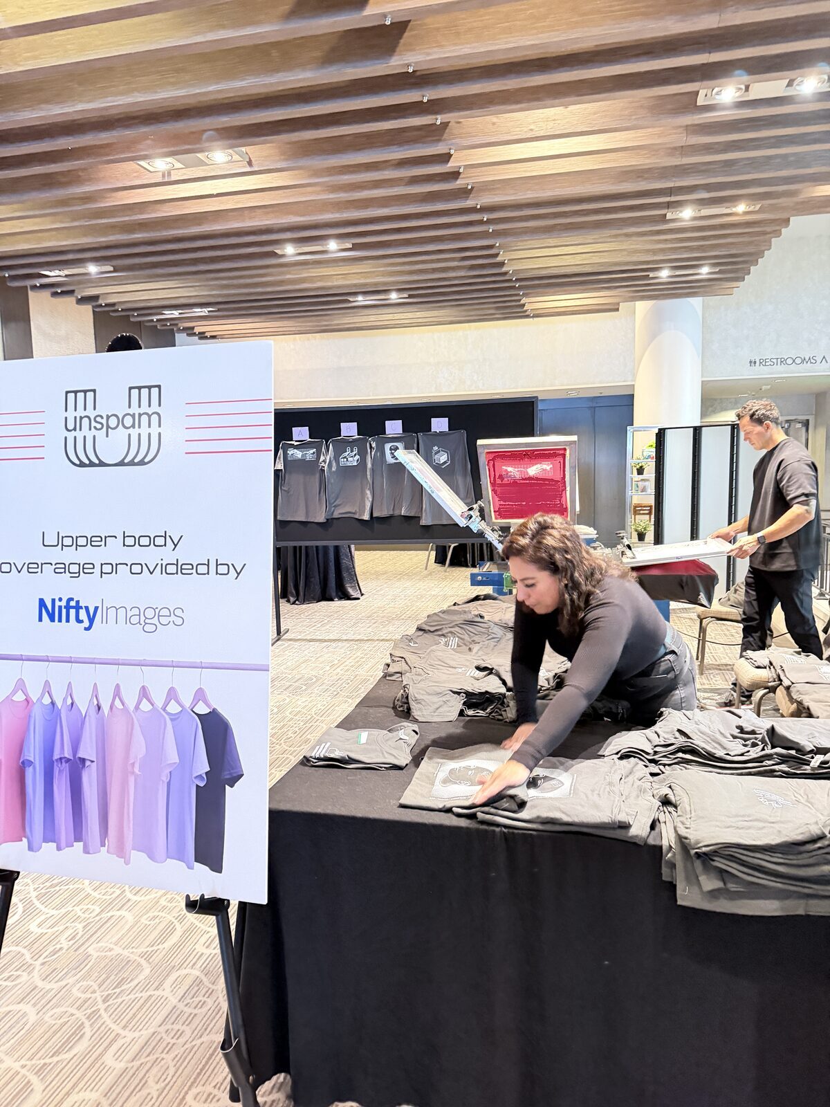 Garment table and live-print station drawing a crowd on a trade-show floor
